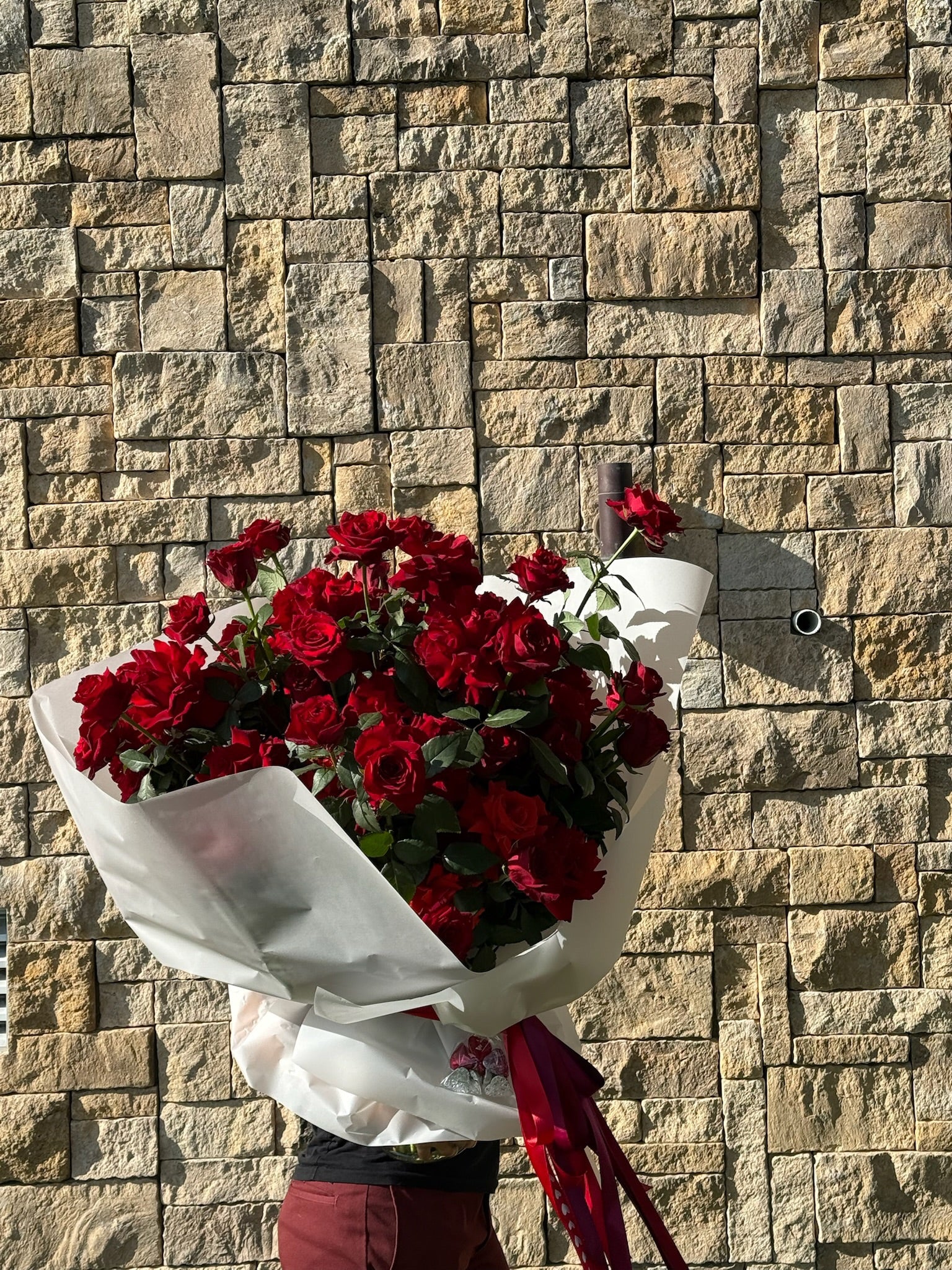 Bouquet of red roses wrapped in white paper against a stone wall.