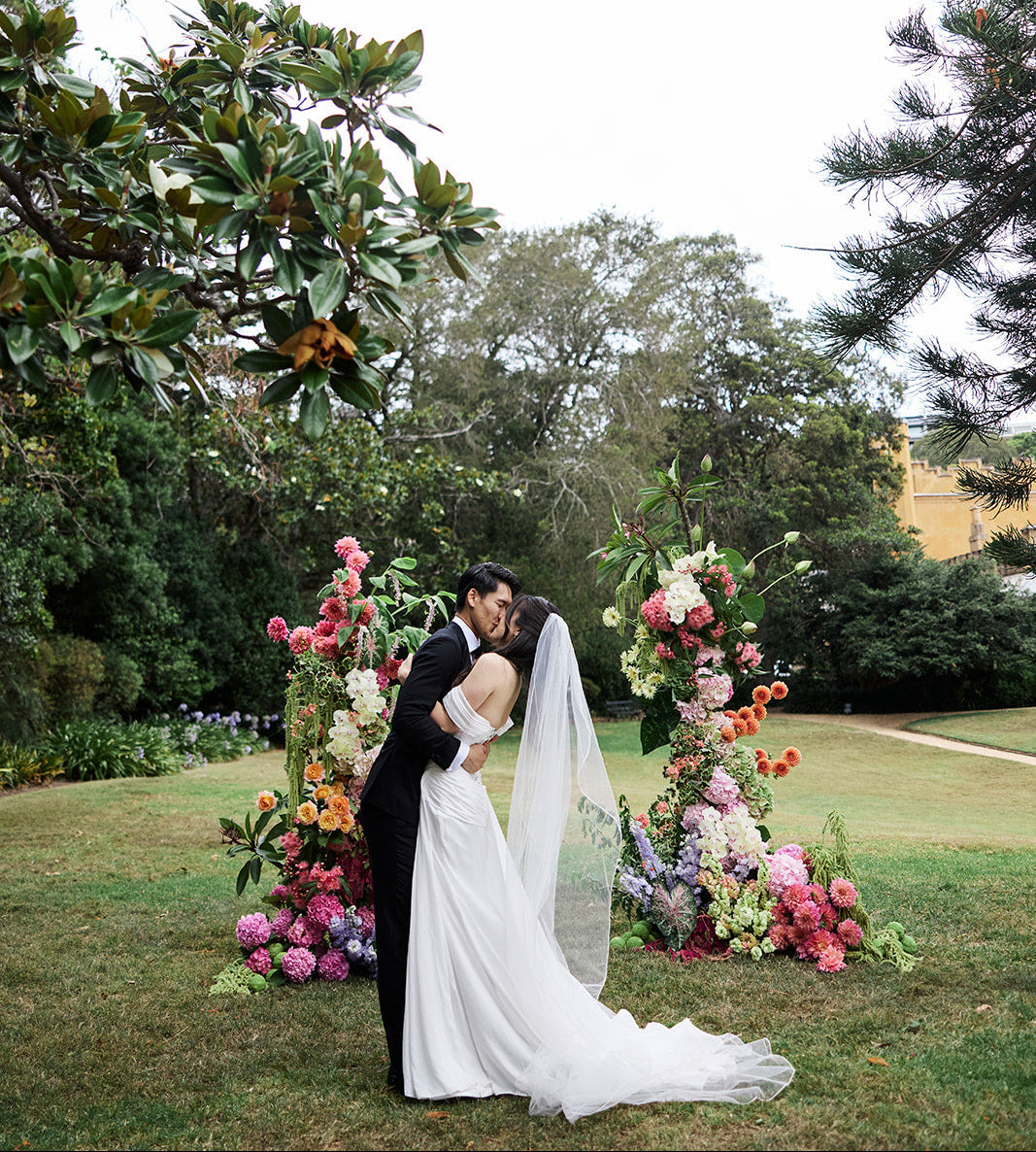 Wedding couple embracing in front of floral arches with greenery