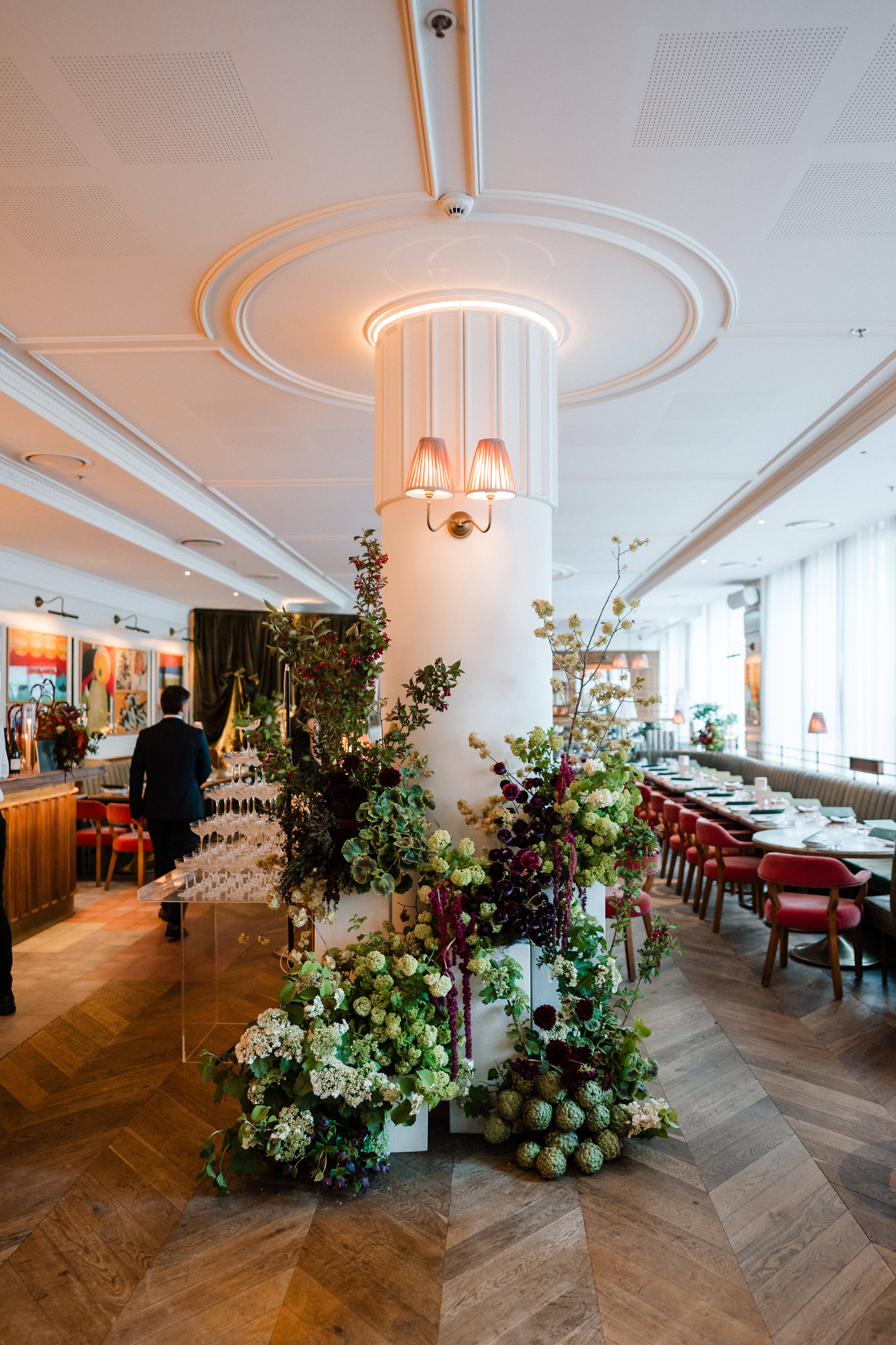 Decorative floral arrangement in a stylish restaurant setting with high ceilings and wooden flooring.